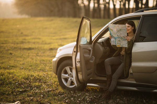 žena sedící v otevřených dveřích auta dívající se do papírové mapy