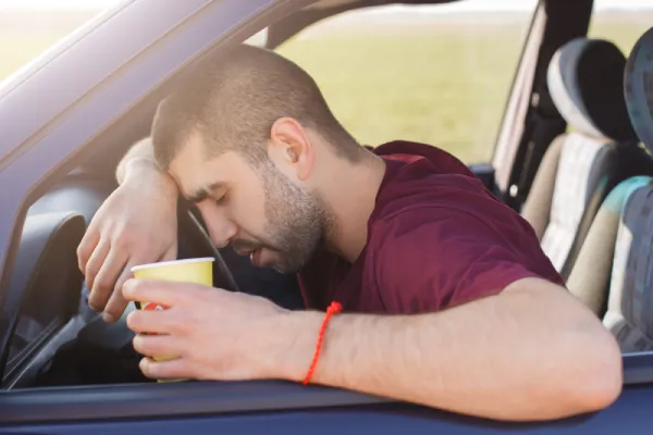 unavený muž s kelímkem kávy v ruce za volantem auta