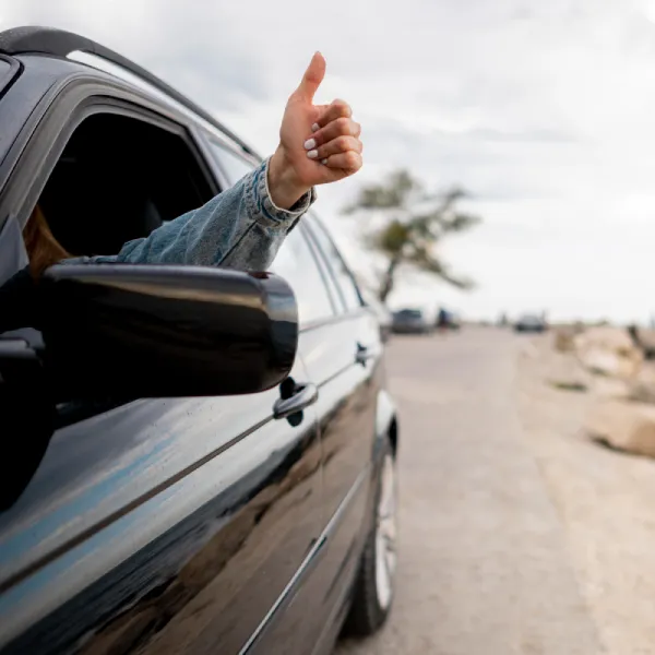 ruka mladé ženy ukazující zdvižený palec z otevřeného okénka auta