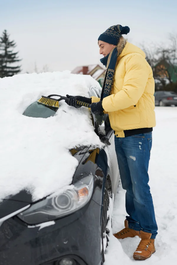 muž čistící čelní sklo auta od sněhu