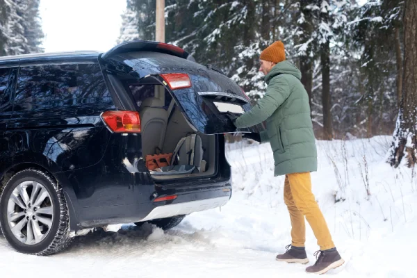 řidič zavírající kufr auta stojícího v zimě na sněhu u lesa